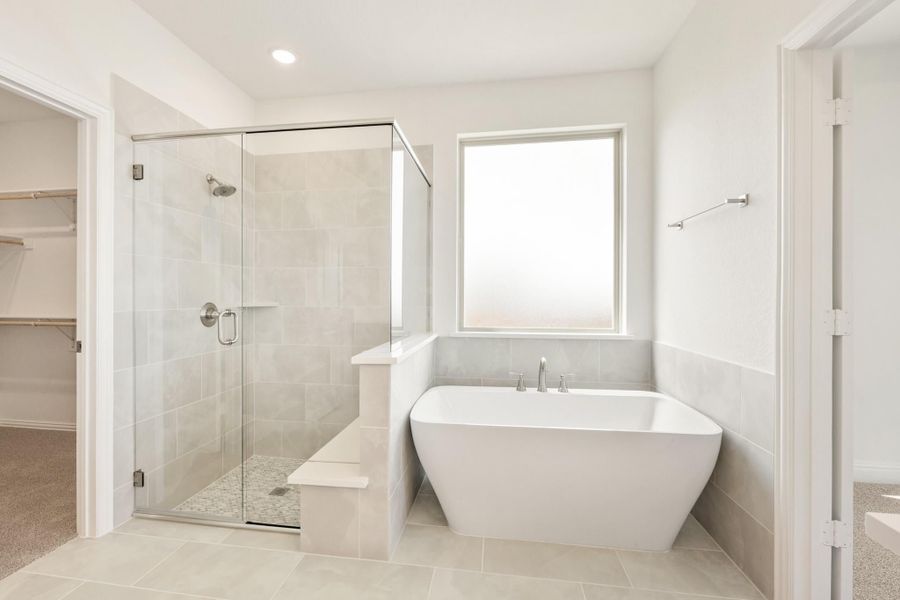 Master bathroom with freestanding soaking tub, glass-enclosed tile shower, and walk-in closet access Master bathroom with freestanding soaking tub, glass-enclosed tile shower, and walk-in closet access