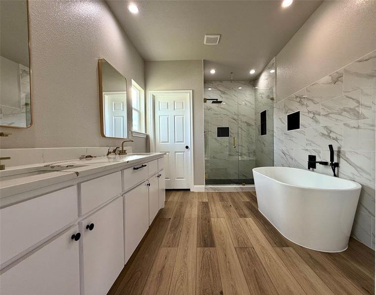 Bathroom featuring double vanity, a marble finish shower, a textured wall, a freestanding tub, and dark wood finished floors