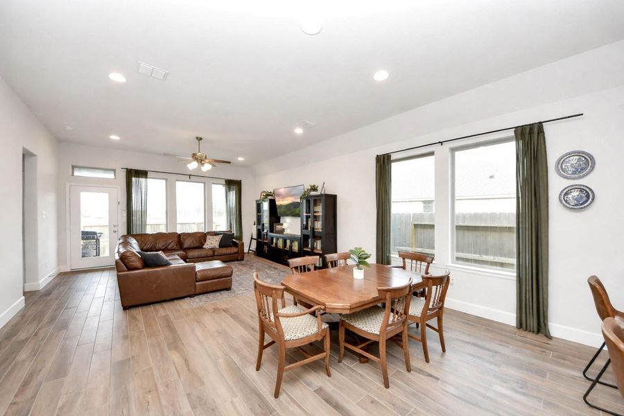 This expansive open-concept living space is filled with natural light and designed for effortless living and entertaining. Rich hardwood floors, a comfortable sectional seating area, and seamless flow into the dining space and modern kitchen with stainless steel appliances create a refined yet welcoming environment for gatherings.