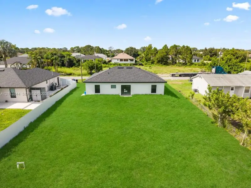 Expansive rear lawn with perimeter vinyl fencing and a dark-toned shingled hip roof Expansive rear lawn with perimeter vinyl fencing and a dark-toned shingled hip roof