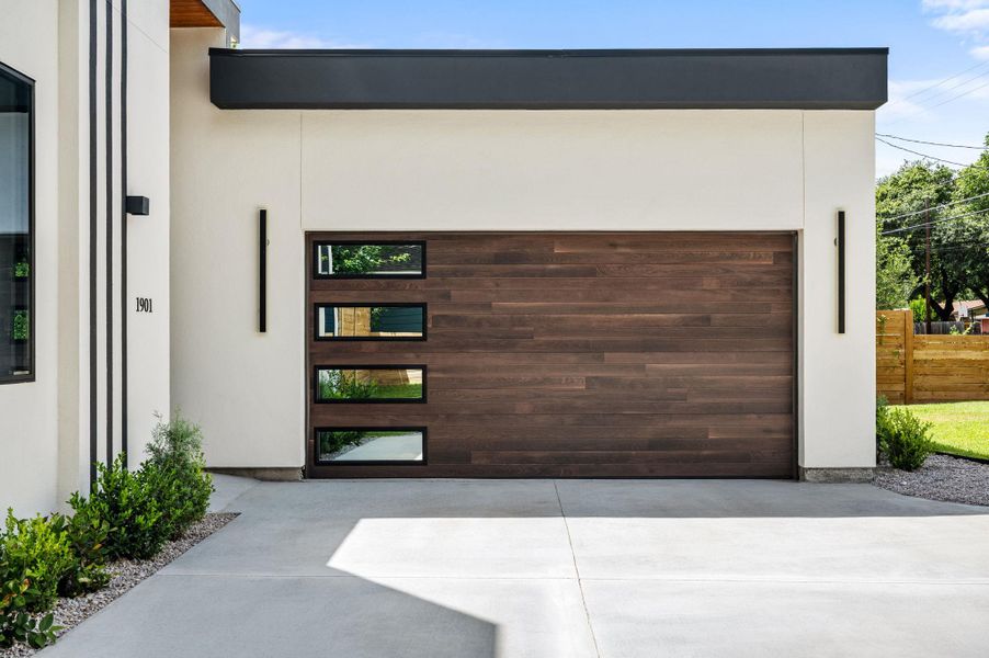 A sleek wood-paneled garage door with horizontal windows complements the contemporary facade and concrete driveway. A sleek wood-paneled garage door with horizontal windows complements the contemporary facade and concrete driveway.