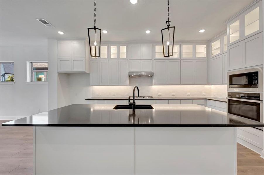 Kitchen with light wood-style flooring, an island with sink, glass insert cabinets, stainless steel appliances, and white cabinets
