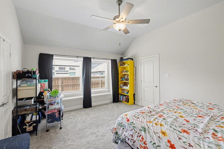 Carpeted room featuring a vaulted ceiling with a ceiling fan, a series of three windows with a built-in sill, and a paneled interior door