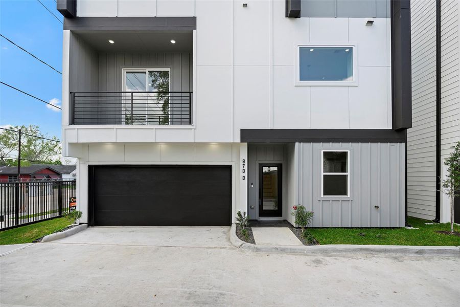 Modern three-story townhouse with a sleek facade, featuring a two-car garage and a small balcony. The entrance is framed by clean lines and minimalistic landscaping, offering a contemporary urban living vibe.