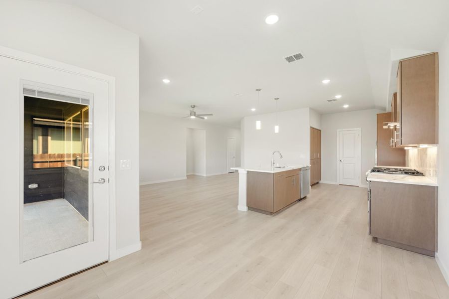 Open-concept kitchen and living area with wood cabinets, center island, and light hardwood floors