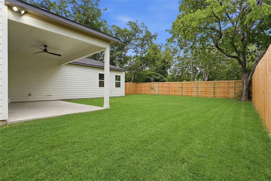Expansive rear yard featuring a large concrete patio, covered outdoor living space with ceiling fan, new wood privacy fencing, and mature trees beyond Expansive rear yard featuring a large concrete patio, covered outdoor living space with ceiling fan, new wood privacy fencing, and mature trees beyond