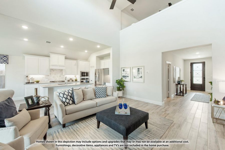 Open-concept living room with high ceilings, hardwood floors, and view into white kitchen with stainless appliances