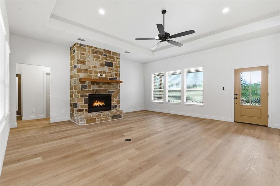 Unfurnished living room featuring a tray ceiling, light wood-style flooring, a fireplace, and ceiling fan Unfurnished living room featuring a tray ceiling, light wood-style flooring, a fireplace, and ceiling fan