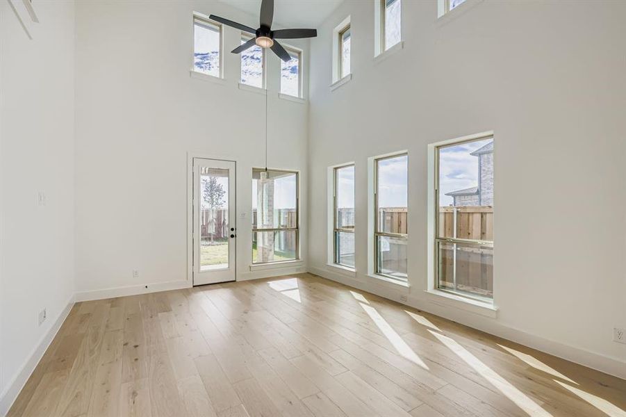 Unfurnished living room with light wood-style flooring, a towering ceiling, and a ceiling fan Unfurnished living room with light wood-style flooring, a towering ceiling, and a ceiling fan