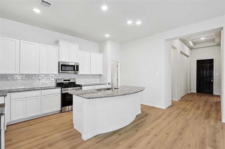 Kitchen featuring light hardwood / wood-style floors, a center island with sink, backsplash, white cabinetry, and appliances with stainless steel finishes