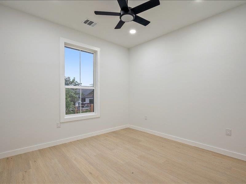This room features light-colored flooring, a window with white trim, and a ceiling fan with a recessed light fixture