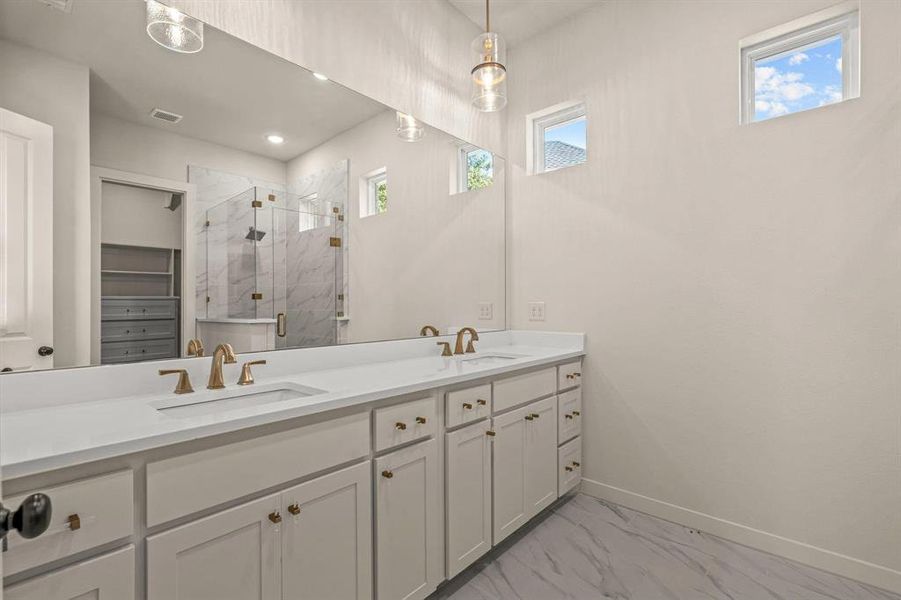 Bathroom featuring marble finish flooring, a marble finish shower, double vanity, and baseboards