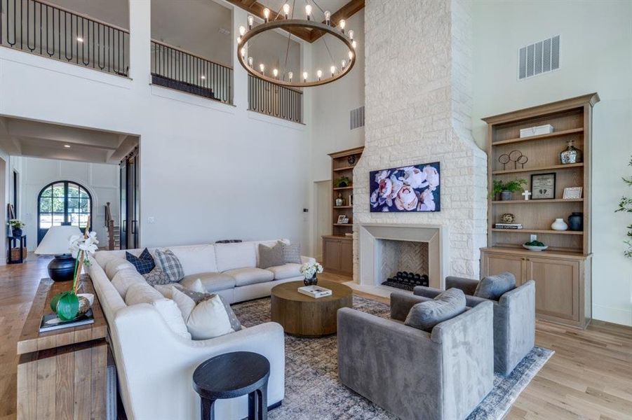 Living room featuring light wood-style floors, a fireplace, built in features, a chandelier, and a high ceiling Living room featuring light wood-style floors, a fireplace, built in features, a chandelier, and a high ceiling