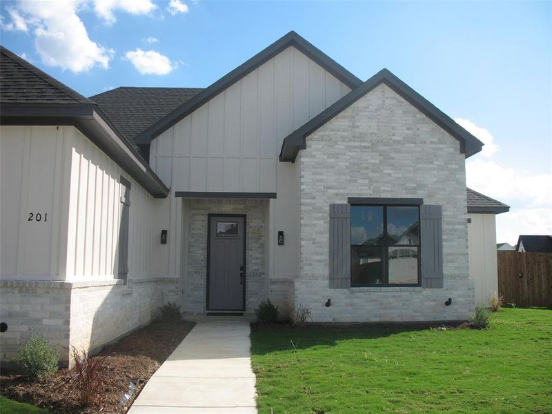 View of front of house featuring board and batten siding, brick siding, and a shingled roof