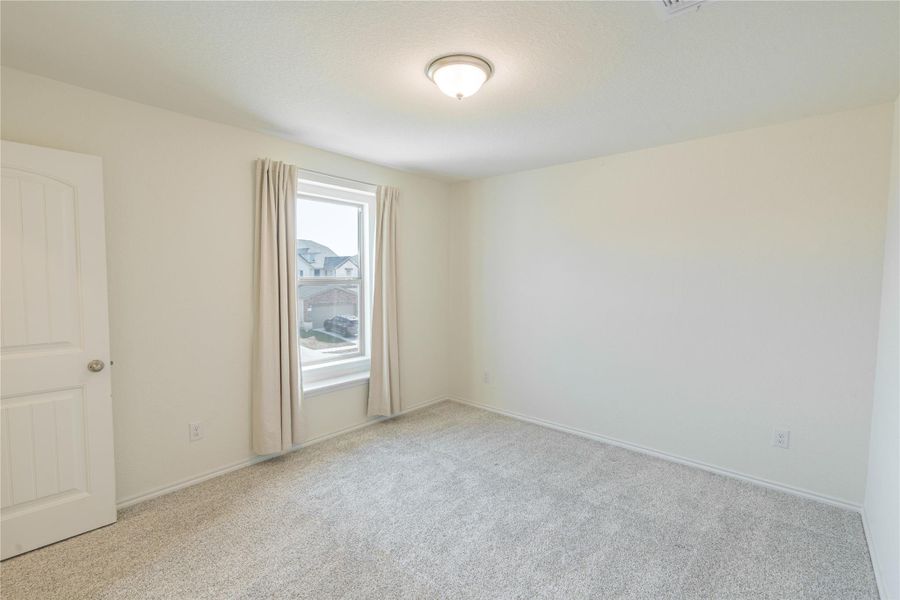A well-lit bedroom with soft carpeting and a window offering a glimpse of the neighborhood. A well-lit bedroom with soft carpeting and a window offering a glimpse of the neighborhood.