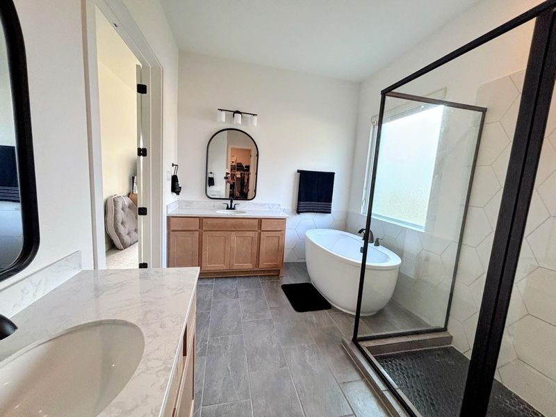 This modern master bathroom features a spacious walk-in shower, a freestanding bathtub, dual sinks with elegant countertops, and stylish fixtures, creating a sleek and inviting atmosphere.