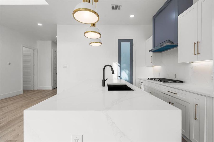 Kitchen with light stone counters, an island with sink, white cabinets, and hanging light fixtures Kitchen with light stone counters, an island with sink, white cabinets, and hanging light fixtures