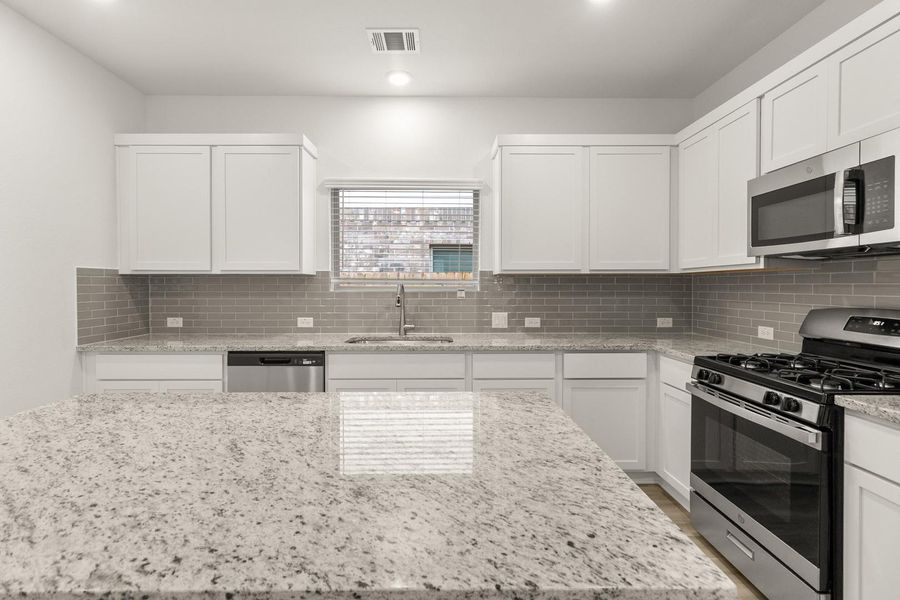 The kitchen features granite countertops, white cabinetry, a grey subway tile backsplash, and stainless steel appliances including a built-in microwave, gas range, and dishwasher