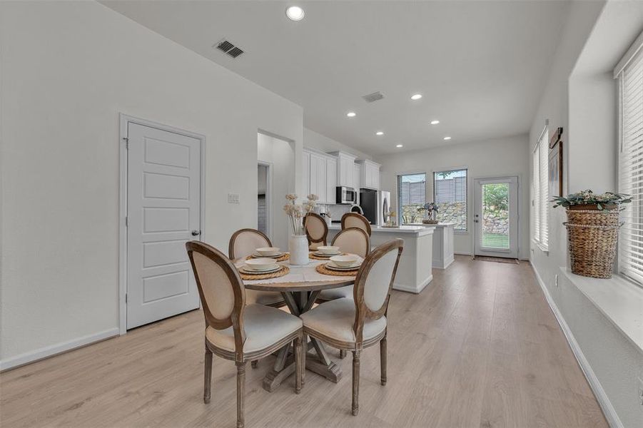 Open-concept dining and kitchen area featuring wood-finish flooring, recessed lighting, white cabinetry, and a glass-paneled door leading to the exterior Open-concept dining and kitchen area featuring wood-finish flooring, recessed lighting, white cabinetry, and a glass-paneled door leading to the exterior