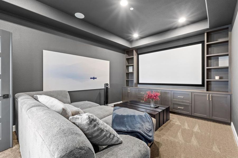 Home theater room featuring light colored carpet, built in shelves, a tray ceiling, and recessed lighting Home theater room featuring light colored carpet, built in shelves, a tray ceiling, and recessed lighting
