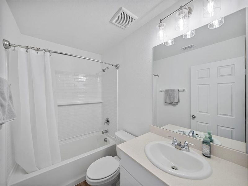 Full bath featuring toilet, shower / bath combo, visible vents, and vanity
