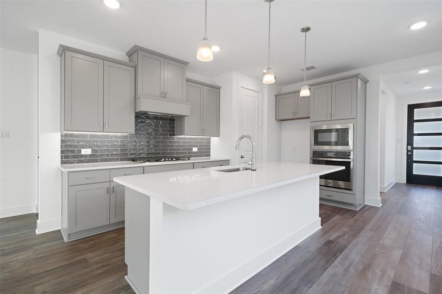 Kitchen with appliances with stainless steel finishes, dark hardwood / wood-style flooring, sink, gray cabinets, and an island with sink