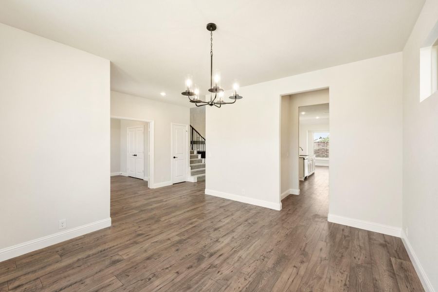 Empty dining room with dark hardwood floors, chandelier, and open view to staircase and kitchen