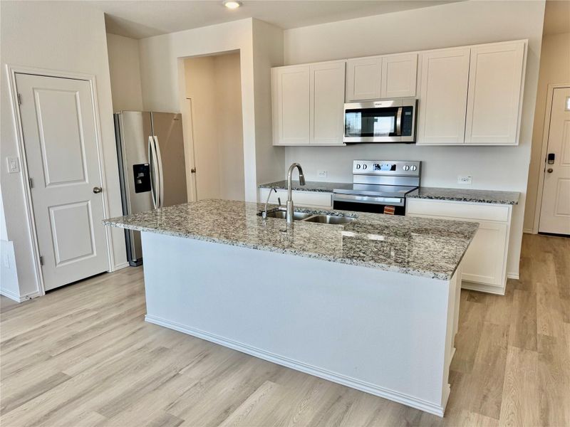 Kitchen featuring appliances with stainless steel finishes, white cabinetry, light stone countertops, a kitchen island with sink, and light wood-style flooring