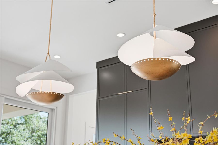 Layered pendant fixtures with soft, flowing forms and warm metallic accents introduce an artistic focal point above the island. Their refined composition adds movement and visual interest, elevating the kitchen’s modern, design-forward aesthetic.