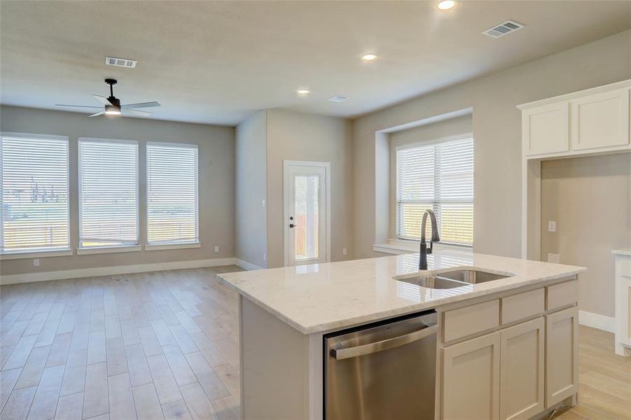 Kitchen featuring dishwasher, light wood-style floors, light stone counters, open floor plan, and a center island with sink