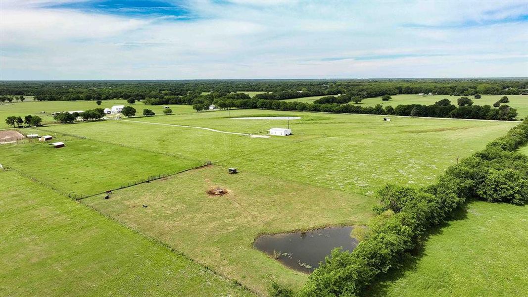 Expansive green acreage featuring a large pond and distant residential structures
