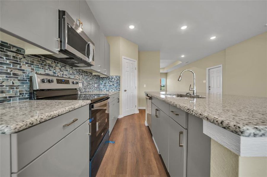 Kitchen with appliances with stainless steel finishes, tasteful backsplash, gray cabinetry, hardwood / wood-style floors, and light stone counters