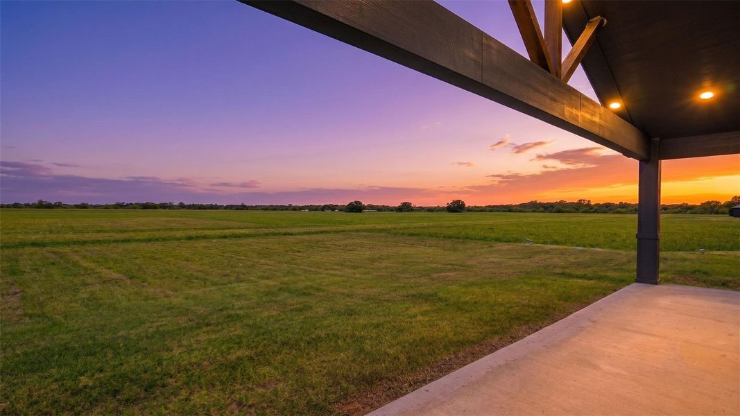 Enjoy wide-open views and expansive skies from the back porch, offering a peaceful setting to relax and take in the surrounding countryside. Twilight image digitally enhanced.