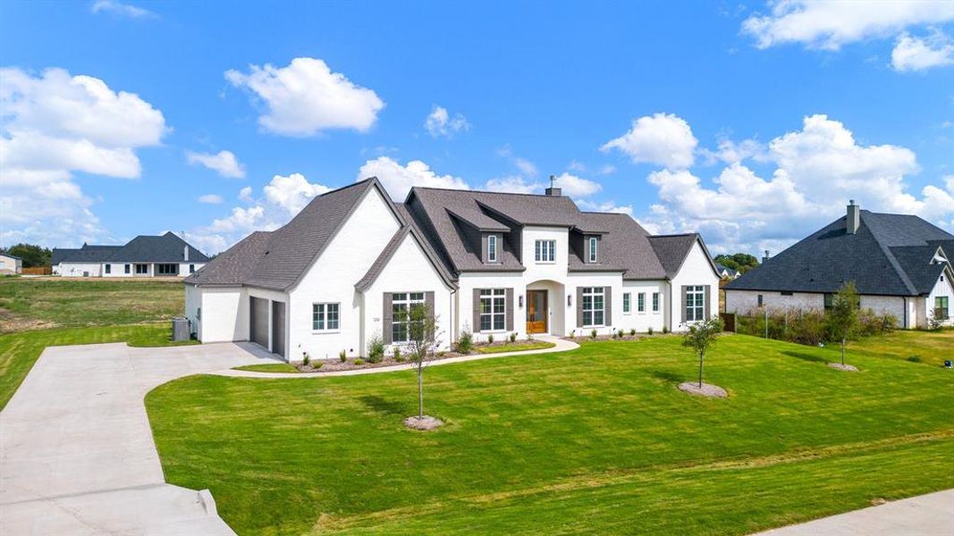 French country inspired facade featuring a garage and a front lawn