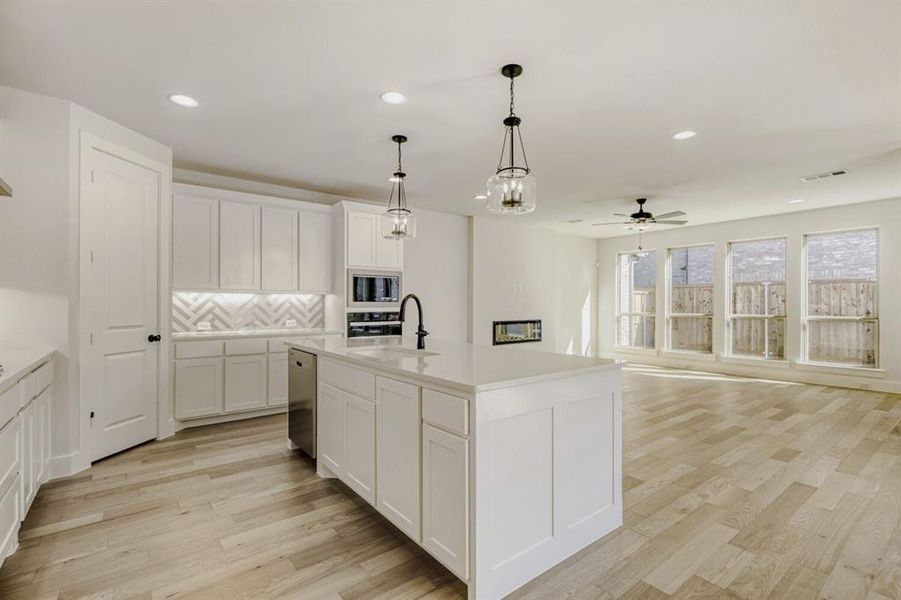 Kitchen with a kitchen island with sink, light wood-type flooring, suspended lighting, a ceiling fan, and open floor plan