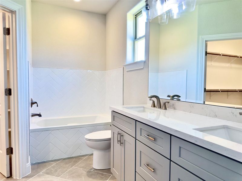 Full bathroom featuring tiled bath, double vanity, tile patterned flooring, and a spacious closet Full bathroom featuring tiled bath, double vanity, tile patterned flooring, and a spacious closet