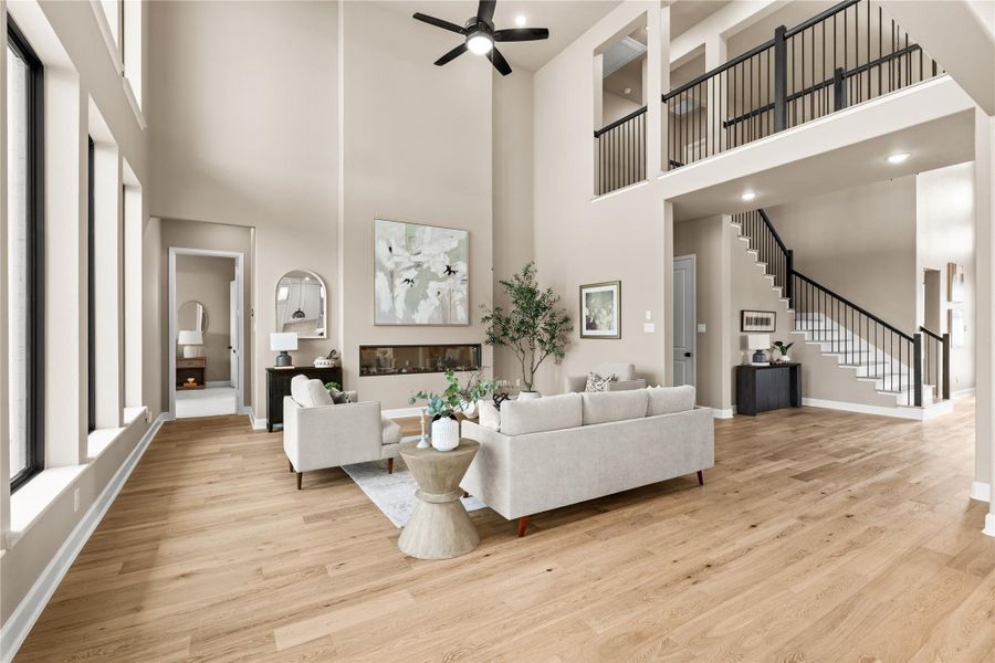 Expansive living area with soaring ceilings, elegant hardwood floors, and a modern fireplace, complemented by a stylish open staircase and abundant natural light. *Virtually Staged*