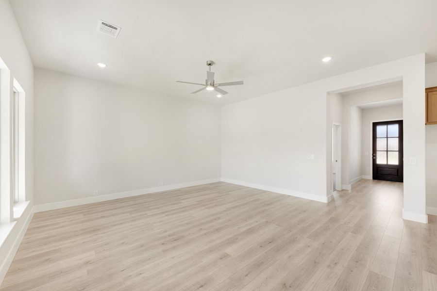 Empty living room with light wood floors, white walls, ceiling fan, and view to front entry door Empty living room with light wood floors, white walls, ceiling fan, and view to front entry door