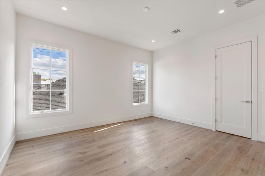 The third secondary bedroom faces the side of the house with two windows to frame a bed perfectly and add warmth to the space. Light walls, hardwoods, and high ceilings continue.