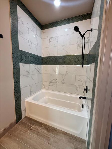 Bathtub and shower combination featuring white subway tile with gray veining, a patterned green accent tile band, and matte black fixtures Bathtub and shower combination featuring white subway tile with gray veining, a patterned green accent tile band, and matte black fixtures