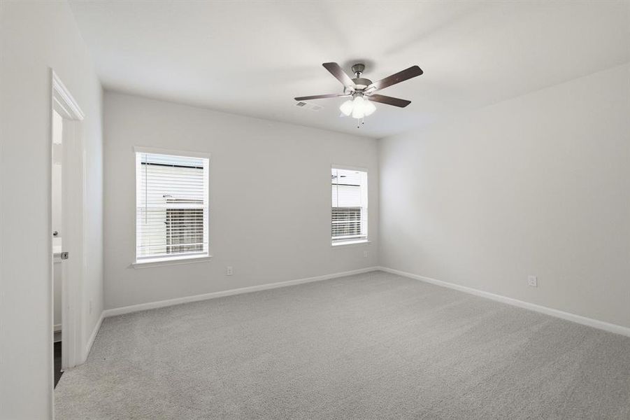 Spacious room featuring light gray carpeting, two windows with blinds, a ceiling fan with light fixture, and a white interior door