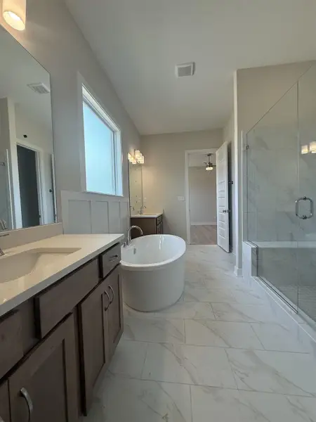 Full bath with a marble finish shower, two vanities, a freestanding tub, and light marble finish flooring