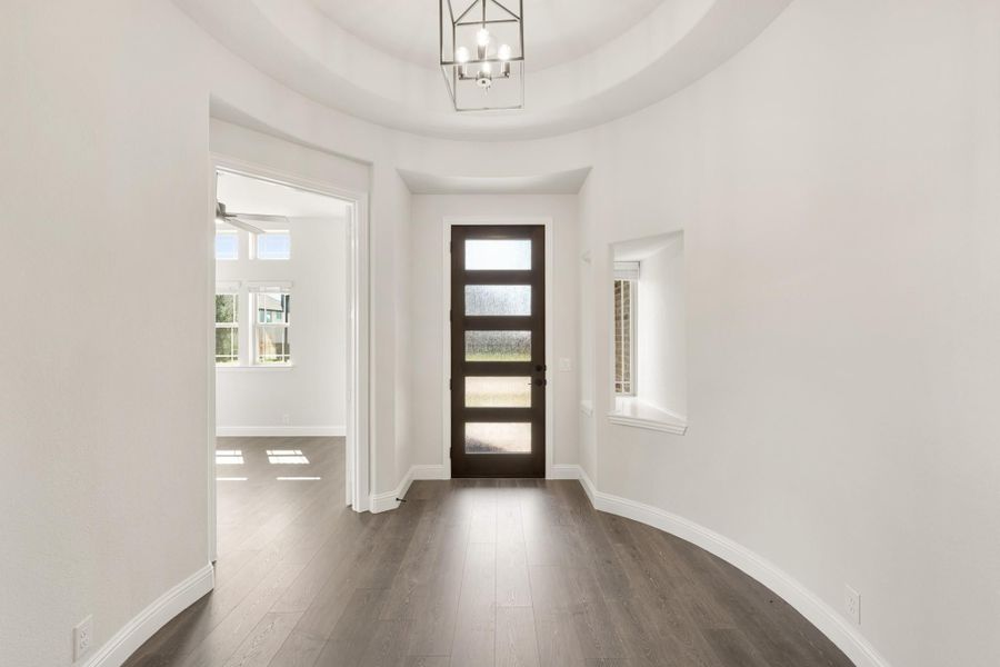 Entryway with dark wood front door, tray ceiling, chandelier, and hardwood floors Entryway with dark wood front door, tray ceiling, chandelier, and hardwood floors