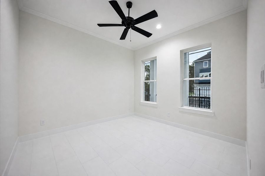 This bright bedroom features clean neutral walls, large-format light tile flooring, crown molding, recessed lighting, and a bold black ceiling fan. Two tall windows bring in natural light and create an airy feel, while the spacious rectangular layout provides flexibility for bedroom furniture, a home office setup, or a comfortable guest retreat. This bright bedroom features clean neutral walls, large-format light tile flooring, crown molding, recessed lighting, and a bold black ceiling fan. Two tall windows bring in natural light and create an airy feel, while the spacious rectangular layout provides flexibility for bedroom furniture, a home office setup, or a comfortable guest retreat.