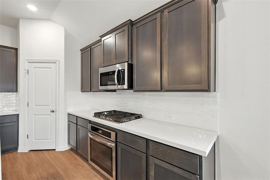 Kitchen with tasteful backsplash, dark brown cabinets, stainless steel appliances, light wood-style flooring, and light stone counters Kitchen with tasteful backsplash, dark brown cabinets, stainless steel appliances, light wood-style flooring, and light stone counters