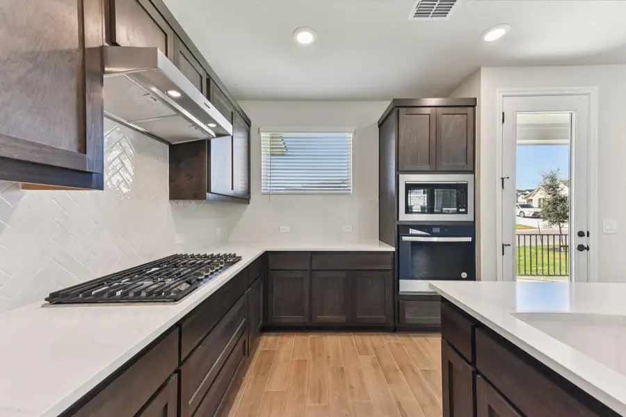 Kitchen with dark brown cabinets, decorative backsplash, healthy amount of natural light, light wood finished floors, and recessed lighting