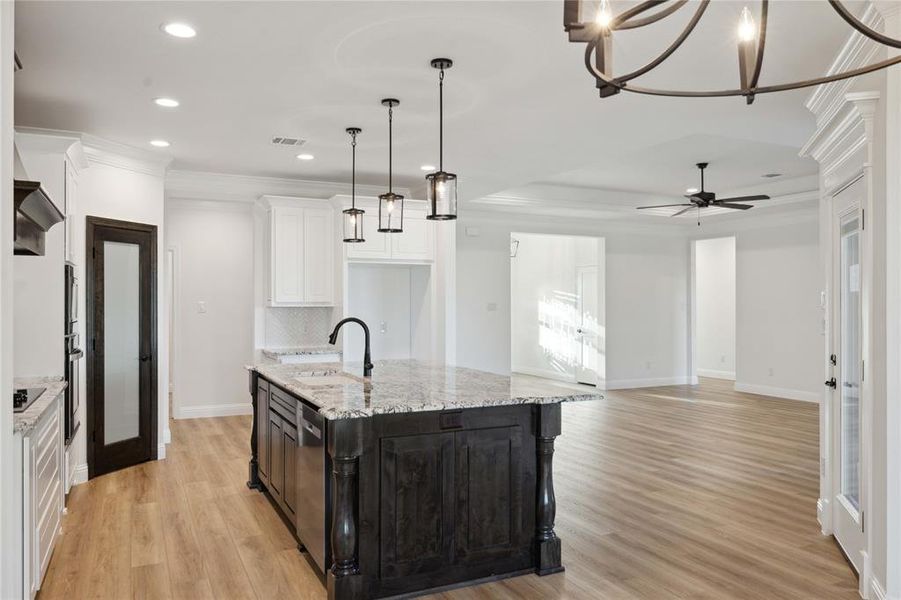 Kitchen with decorative light fixtures, light hardwood / wood-style flooring, backsplash, and an island with sink