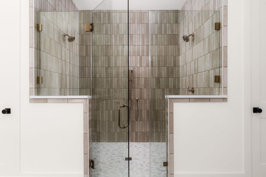 Step into a spacious, well-lit walk-in shower with modern tile and dual showerheads.