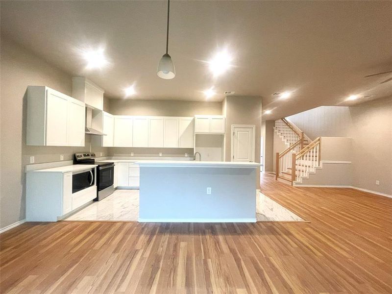Kitchen with electric stove, light wood-style flooring, baseboards, and light countertops
