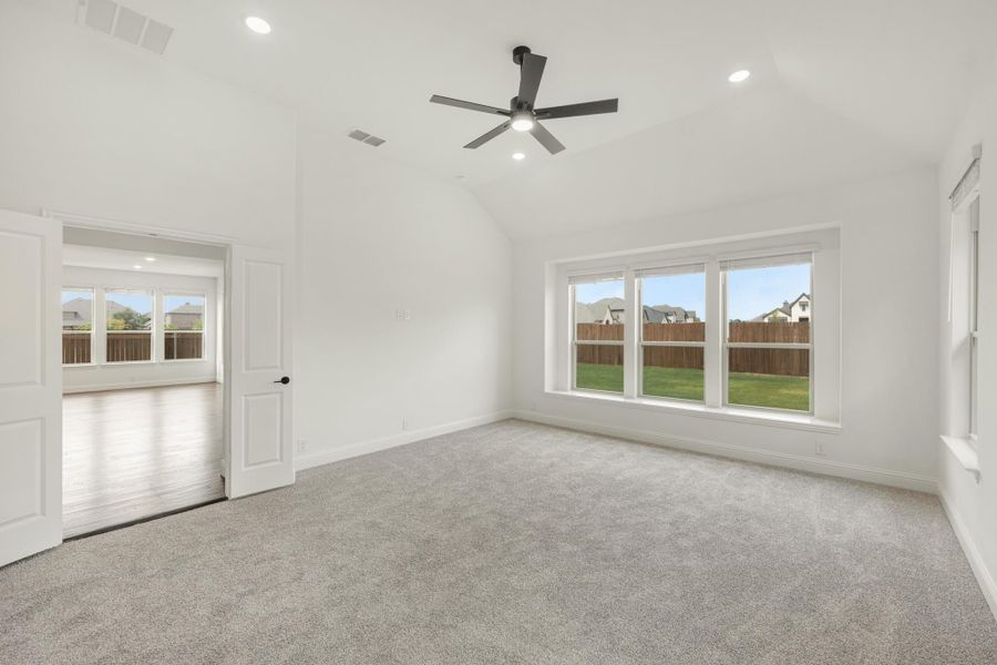 Empty bedroom with vaulted ceiling, ceiling fan, gray carpet, and large windows overlooking backyard
